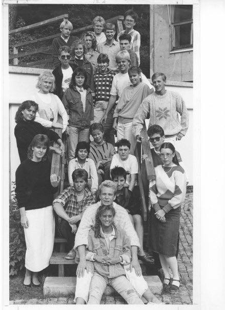 A black and white group photo of a large gathering of young people posing on and around a staircase. The individuals are wearing various styles of clothing from the late 1980s to early 1990s, with some wearing sunglasses and casual attire. The group appears to be a mix of friends or classmates.