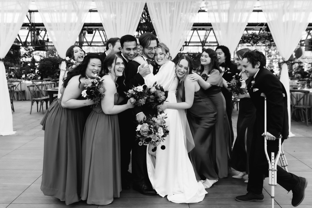 A joyous group of bridesmaids and groomsmen celebrating at a wedding, dressed in elegant outfits and holding bouquets, surrounded by a beautifully decorated venue.