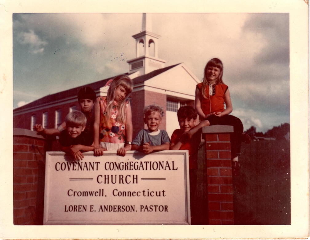 A group of children posing in front of a church sign that reads 'COVENANT CONGREGATIONAL CHURCH, Cromwell, Connecticut'. The church building is visible in the background.